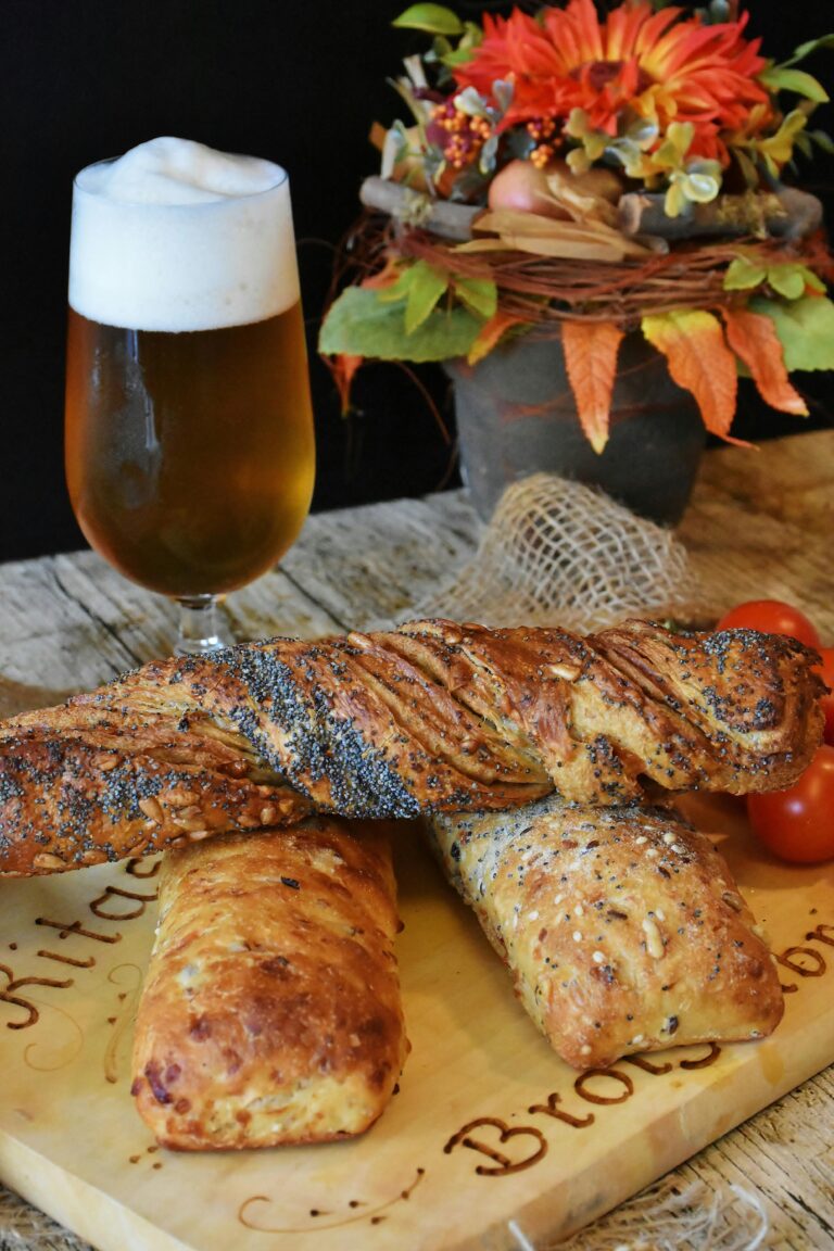 Artisan bread with a frothy beer and autumn flowers on a wooden table.