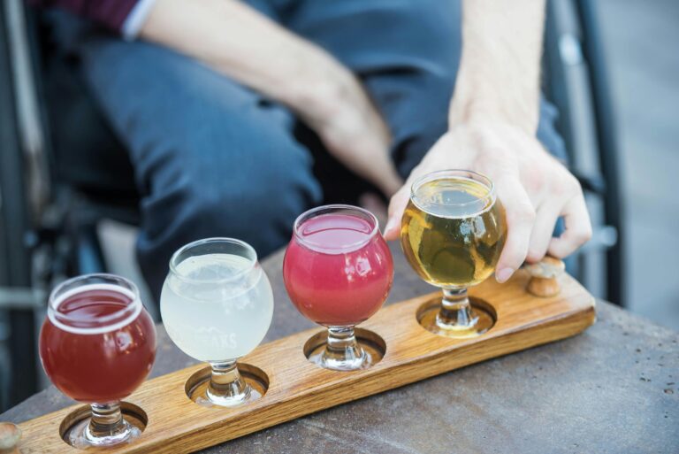 A selection of colorful craft beers served on a wooden paddle with a hand reaching over.