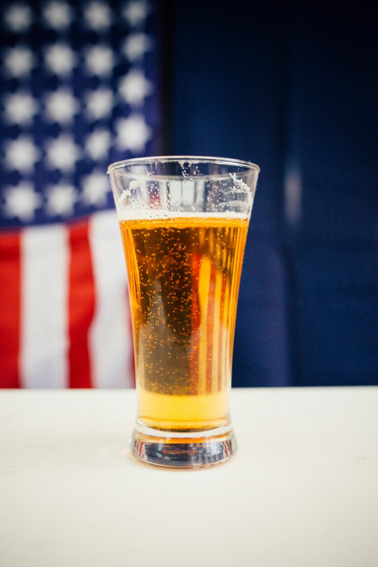 A cold glass of beer against a blurred American flag backdrop, perfect for patriotic themes.