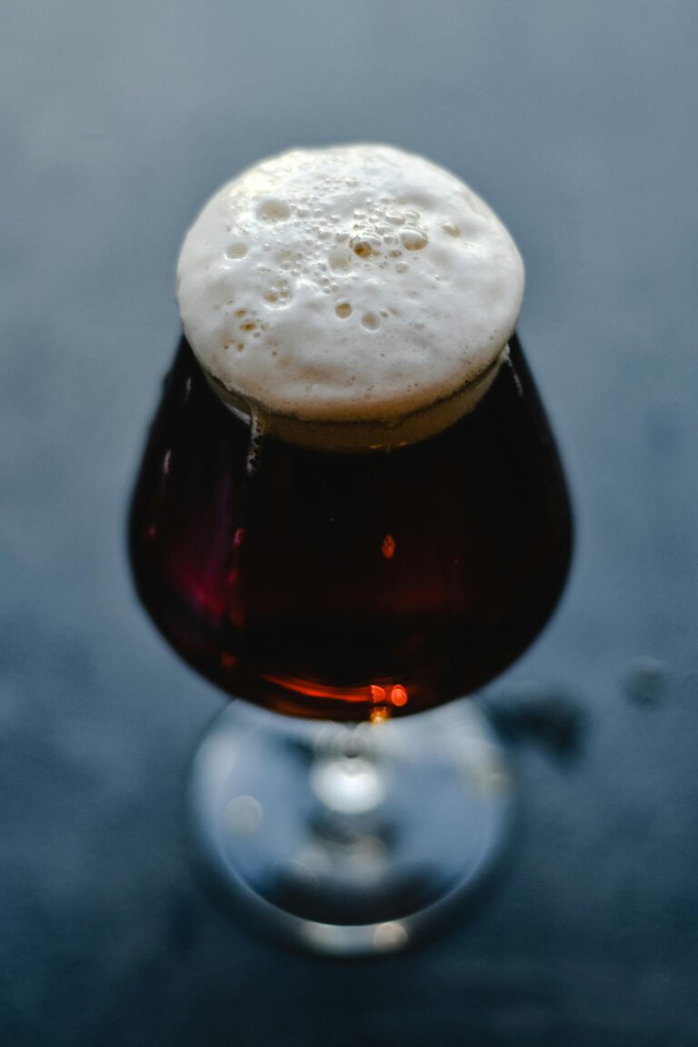 A close-up of a dark beer in a glass with a frothy head, showcasing the rich texture and color.